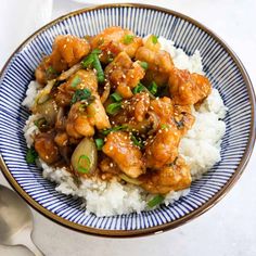 a blue and white bowl filled with chicken, rice and green onions on top of a table