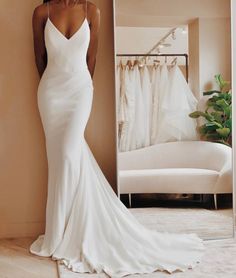 a woman standing in front of a mirror wearing a white wedding dress with spaghetti straps