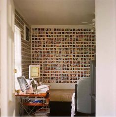 a room with a bed, desk and computer on the table in front of a wall that has pictures all over it