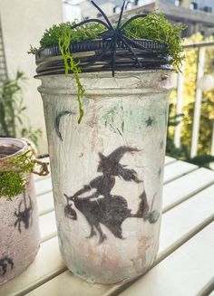 a painted jar sitting on top of a wooden table next to a potted plant