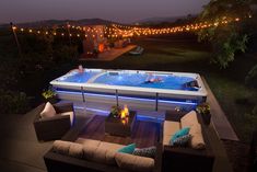 an outdoor hot tub is lit up at night with string lights and furniture around it