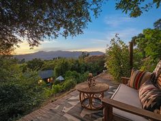 an outdoor seating area overlooks the mountains and trees at sunset or sunrise, as well as a table with two pillows on it