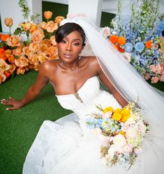 a woman in a wedding dress sitting on the ground with her bouquet and veil over her head