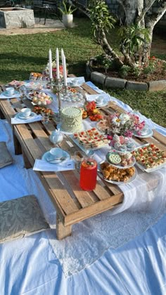 a wooden table topped with lots of food on top of a blue cloth covered ground