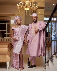 a man and woman in traditional african attire walking down the stairs with chandelier