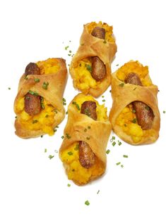 four pastries with sausage and eggs in them sitting on a white surface, ready to be eaten