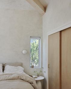 a bed sitting under a window next to a wooden door in a room with white walls