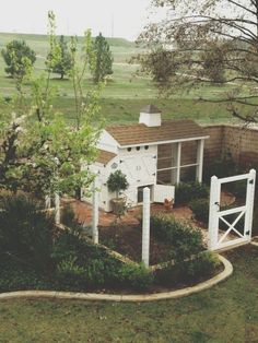 a small white house in the middle of a grassy area with trees and bushes around it