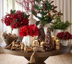 a table topped with lots of vases filled with flowers and pine cones next to candles