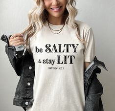 Express your faith with comfort and style in our Be Salty Matthew 5:13 Christian t-shirt. This soft and comfortable unisex shirt is perfect for sharing your beliefs in a fun and trendy way. Available in XS - 3XL Please be sure to view the size chart by scrolling through the photos in the listing. *Side seams, retail fit *Shoulder to shoulder taping *Unisex sizing *Tearaway label Wash inside out with like colors in cold water, do not bleach, or presoak. Tumble dry or hang dry.  **Please be sure t Trending Christian Tshirts, Funny Christian Shirts Humor, Faith Shirts For Women, Christian Sayings For Shirts, Church T Shirt Ideas Design, Matthew 5 13, Jesus Clothes, Christian Shirts Designs, Tee Designs