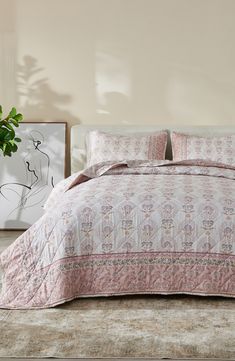 a bed with pink and white bedspread in a bedroom next to a plant