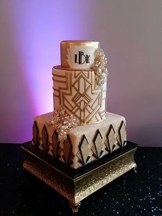 a three - tiered cake is decorated with gold and white decorations on a black table