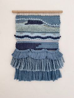 a wall hanging made out of blue yarn and fringes with a wooden hanger