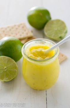 a glass filled with yellow liquid next to limes and crackers