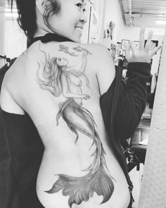 a woman with a mermaid tattoo on her back showing off her large breast and stomach