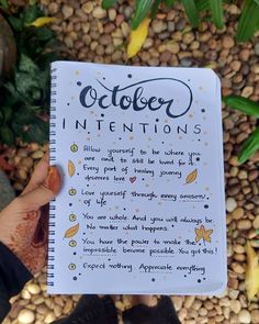 someone holding up a notebook with the words october written on it in front of some rocks