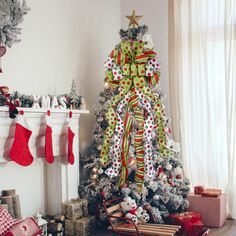 a decorated christmas tree in the corner of a living room with stockings and presents on the fireplace