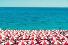 many red and white umbrellas are set up on the beach near the water's edge