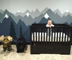 a baby in a crib with mountains painted on the wall behind it and two stuffed animals