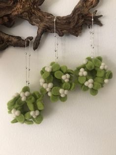 two green and white flowers are hanging from the wall next to a branch with beads on it