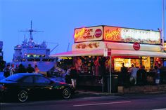 people are standing outside of a restaurant on the side of the road at night time