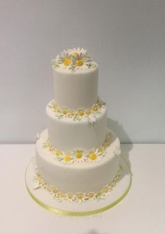 a three tiered white cake with daisies on it