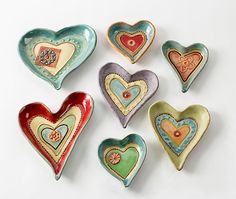 six heart shaped dishes are arranged on a white surface, each with different designs and colors