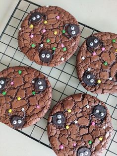 four chocolate cookies decorated with googly eyes and sprinkles on a cooling rack