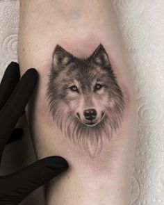 a black and white wolf tattoo on the left leg with a hand next to it