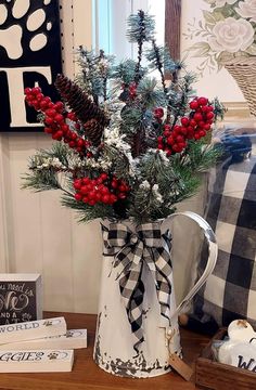 a white pitcher filled with red berries and pine cones on top of a wooden table