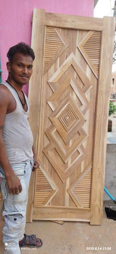 a man standing next to a wooden door in front of a pink wall with an intricate design on it