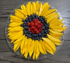 a clear plate topped with bananas, blueberries and raspberries on top of a wooden table