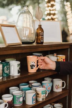 a person is holding a coffee mug in front of shelves full of coffee cups and other items