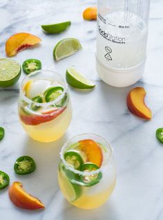 two glasses filled with drinks sitting on top of a table next to limes and peppers