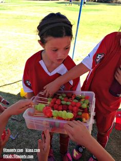 two girls in red shirts are picking up fruit from a plastic container