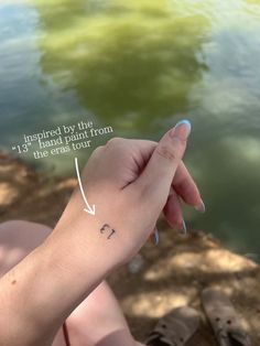 a person with a small tattoo on their wrist pointing at the water's edge