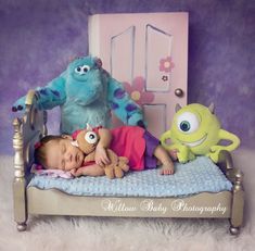 a baby laying in a bed next to two stuffed animals and a toy monster on top of it