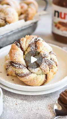 a white plate topped with powdered sugar covered pastry next to a container of nutella