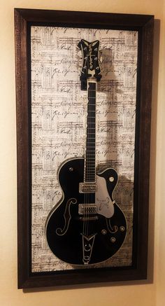 a black and white guitar is hanging on the wall next to a brown framed photograph