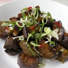 a white plate topped with eggplant, onions and scallion sprouts