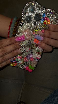 a woman's hand holding a cell phone covered in lots of beads and jewels