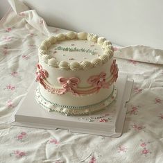 a three layer white cake with pink bows on top sitting on a table next to a book