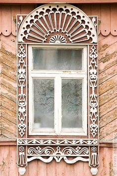 an ornate window on the side of a pink building with wooden shutters and windows