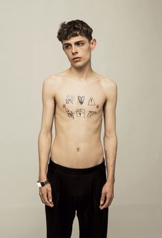 a shirtless man with tattoos on his chest standing in front of a white wall