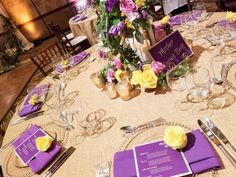 a table with purple and yellow napkins, silverware, and flowers on it