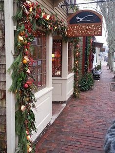 a store front decorated for christmas with garland and lights on the outside wall, along brick walkway