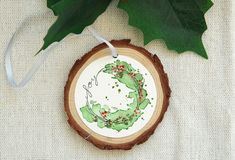 a christmas ornament hanging from a tree slice with holly on it's side