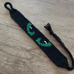 a black bracelet with green letters on it and a tassel hanging from the end