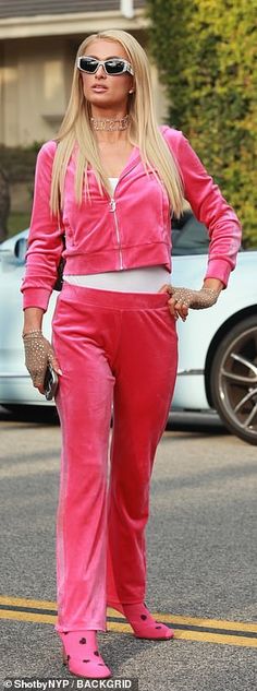 a woman in pink is standing on the street with her hands on her hips and looking at the camera