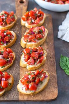 several pieces of bread with tomatoes and herbs on them sitting on a wooden cutting board